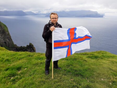 Łukasz Lach na wyspie Kalsoy na Wyspach Owczych, promotor archipelagu i organizator wycieczek na Wyspy Owcze, na tle surowych klifów i latarni, kadr z wycieczki objazdowe